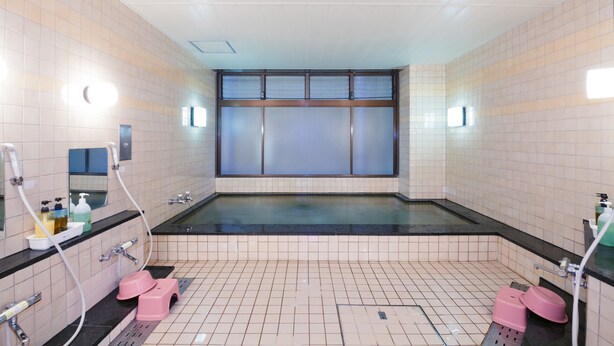 A public restroom with a large bathtub, tiled walls, and a mirror. - Kyoto Travelers Inn (Kyoto)