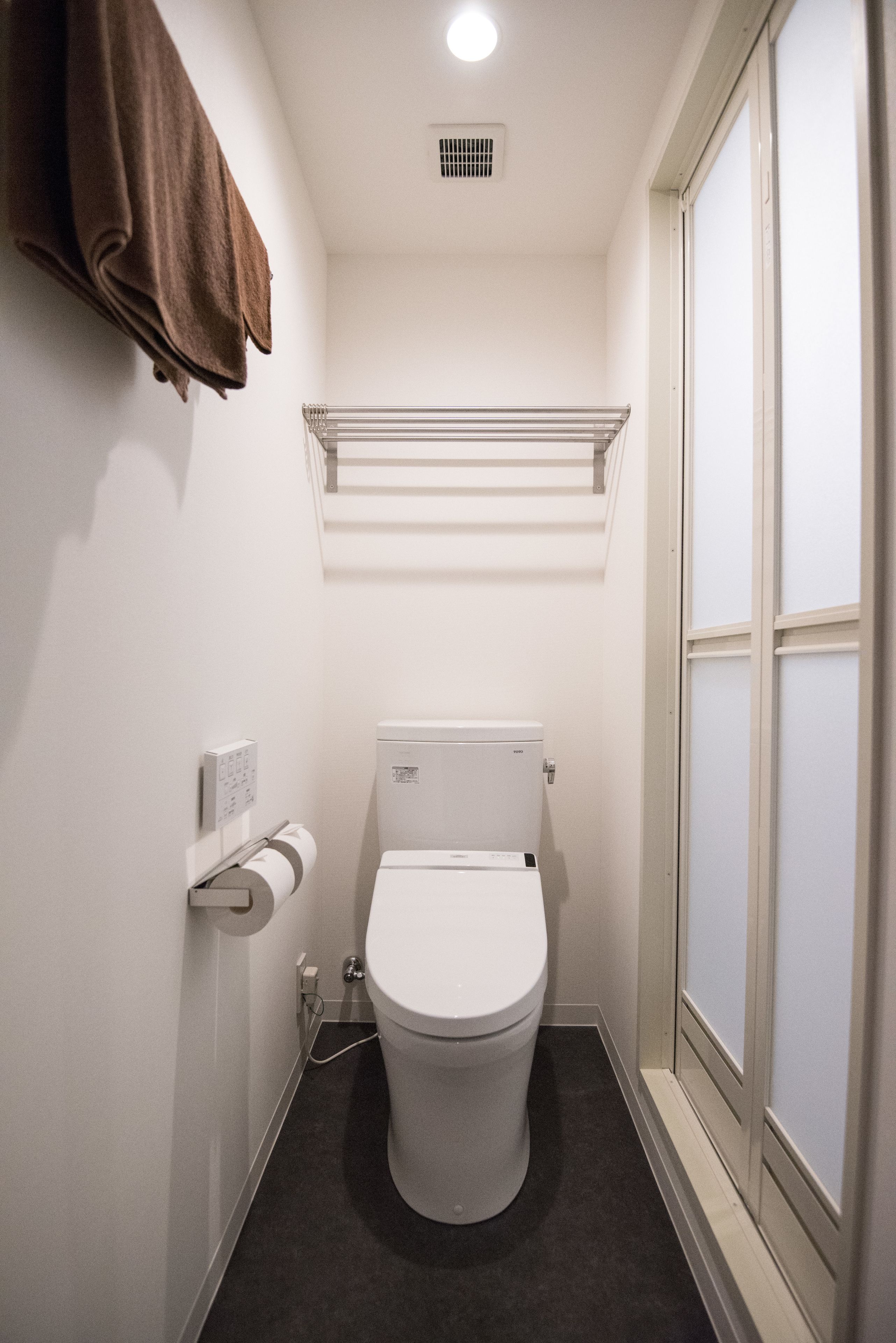 Une petite salle de bain comprenant des toilettes, un porte-serviettes, une étagère au-dessus des toilettes et une fenêtre.
