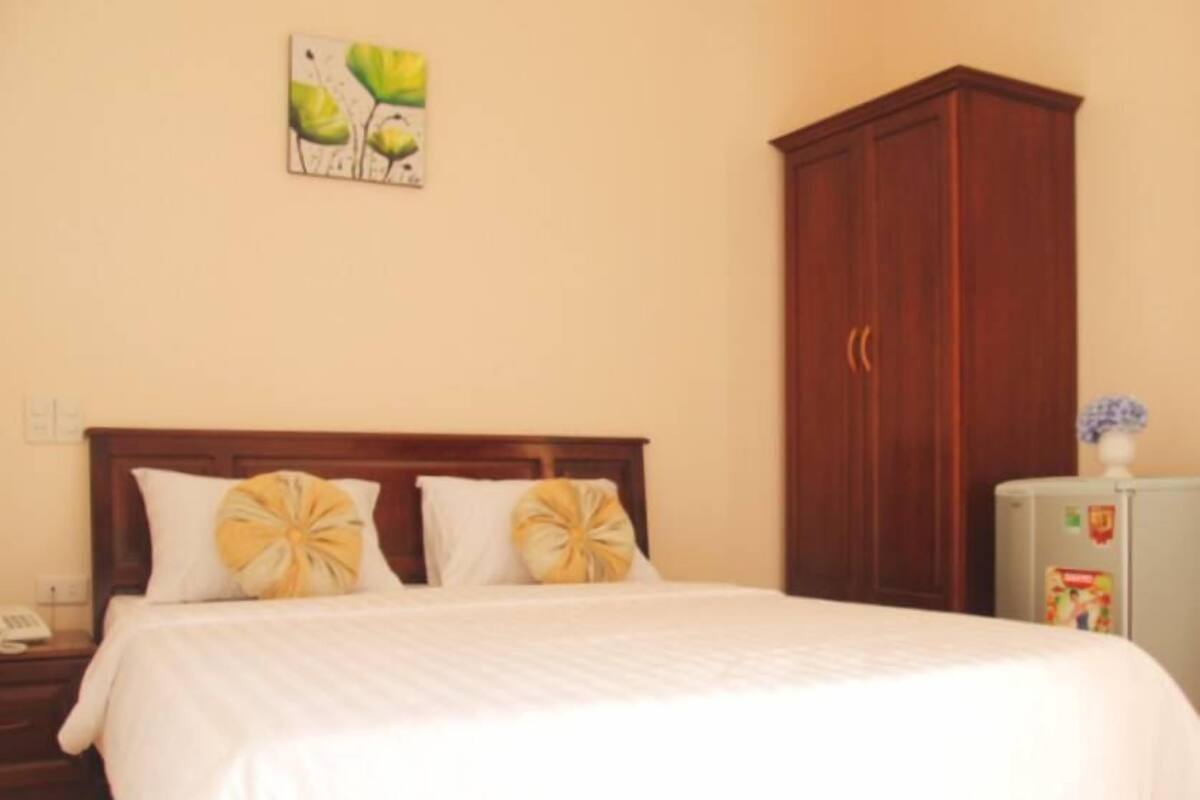 Habitación de hotel con cama de madera, dos almohadas, una mesita de noche, un cuadro colgado en la pared y un armario.