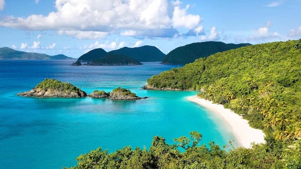 Una playa tropical con aguas turquesas cristalinas, una orilla de arena y colinas verdes exuberantes al fondo.