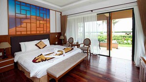 A hotel room with a large bed, a dining table, chairs, a view of the garden, and a painting on the wall. - Blue Bay Mui Ne Resort & Spa (Mui Ne)