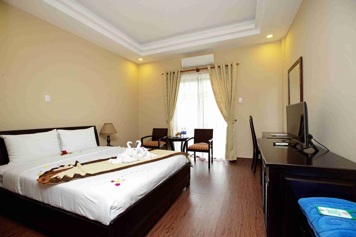 A hotel room with a large bed, a desk with a TV, and a chair.