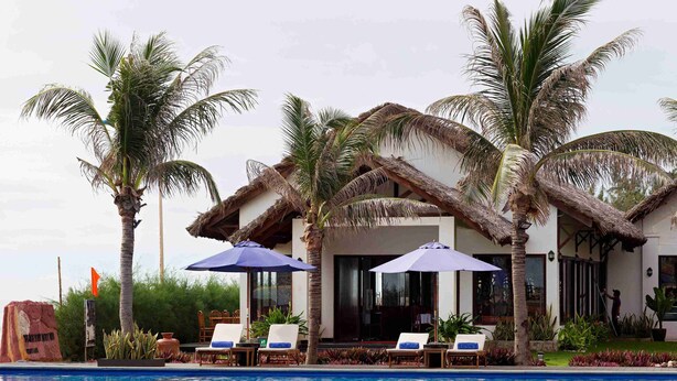 A poolside area with lounge chairs, umbrellas, and a building with a thatched roof. - Blue Bay Mui Ne Resort & Spa (Mui Ne)