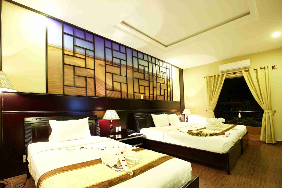 A hotel room with two beds, a decorative wall, a window with curtains, and a night view.