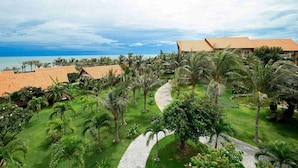 A resort with a paved pathway, palm trees, and buildings with red roofs. - Blue Bay Mui Ne Resort & Spa (Mui Ne)