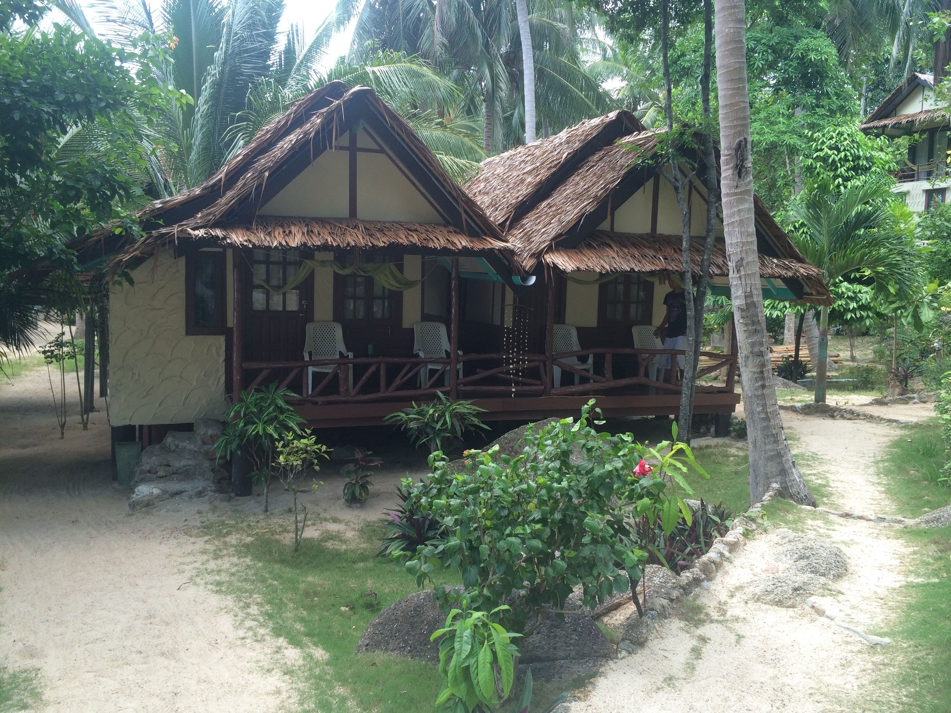 A bungalow with a thatched roof, wooden deck, and a small garden area.