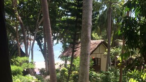 A tropical garden with a thatched-roof building, lush greenery, and a view of the beach. - Smile Bungalows (Ko Pha-ngan)