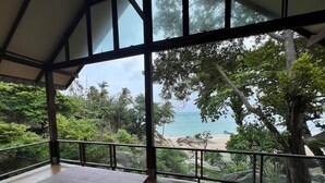 A wooden table in a room with large windows overlooking a beach and tropical vegetation. - Smile Bungalows (Ko Pha-ngan)