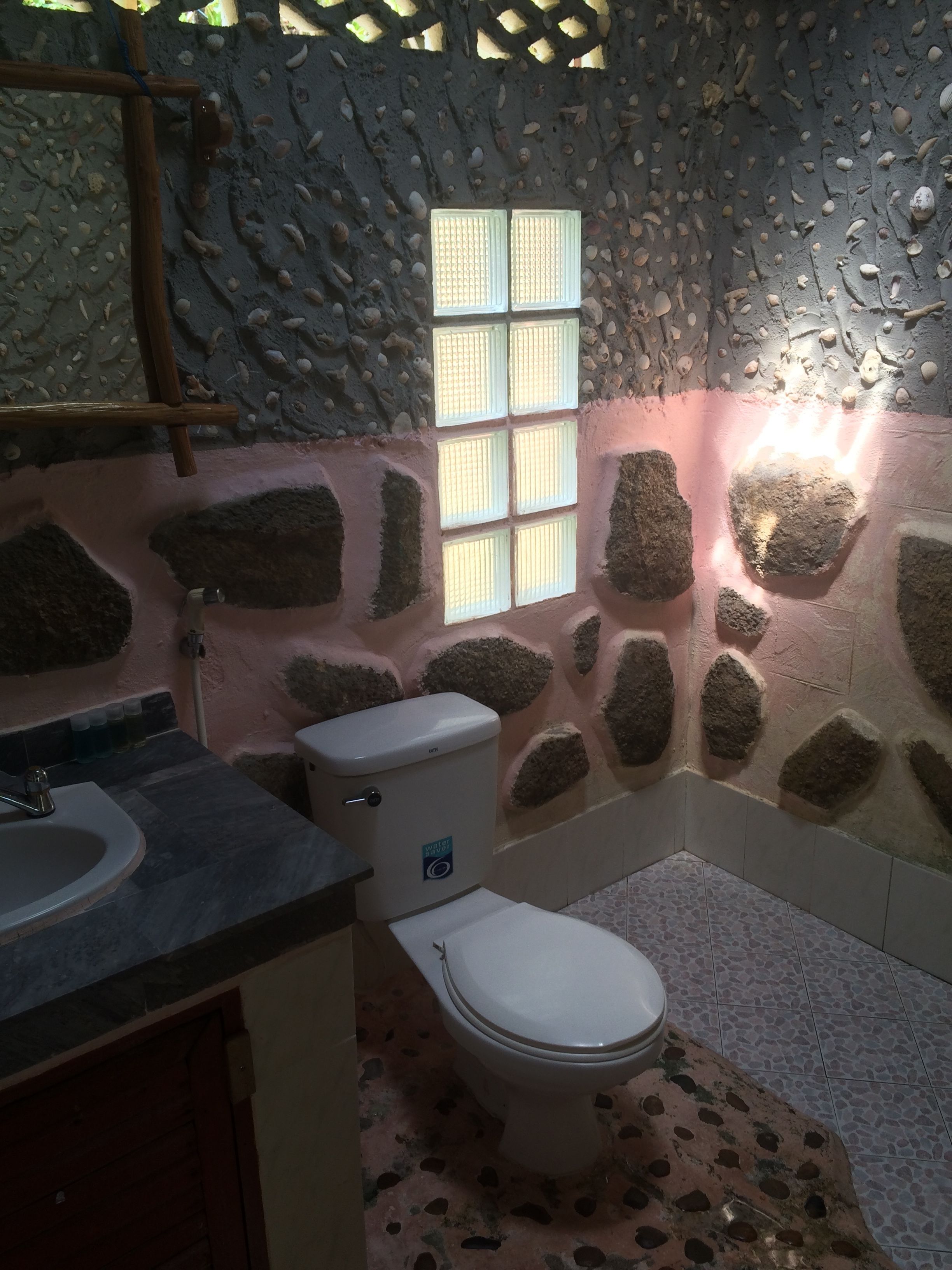 Et badeværelse med stenvæg, et vindue, et toilet og en vask.