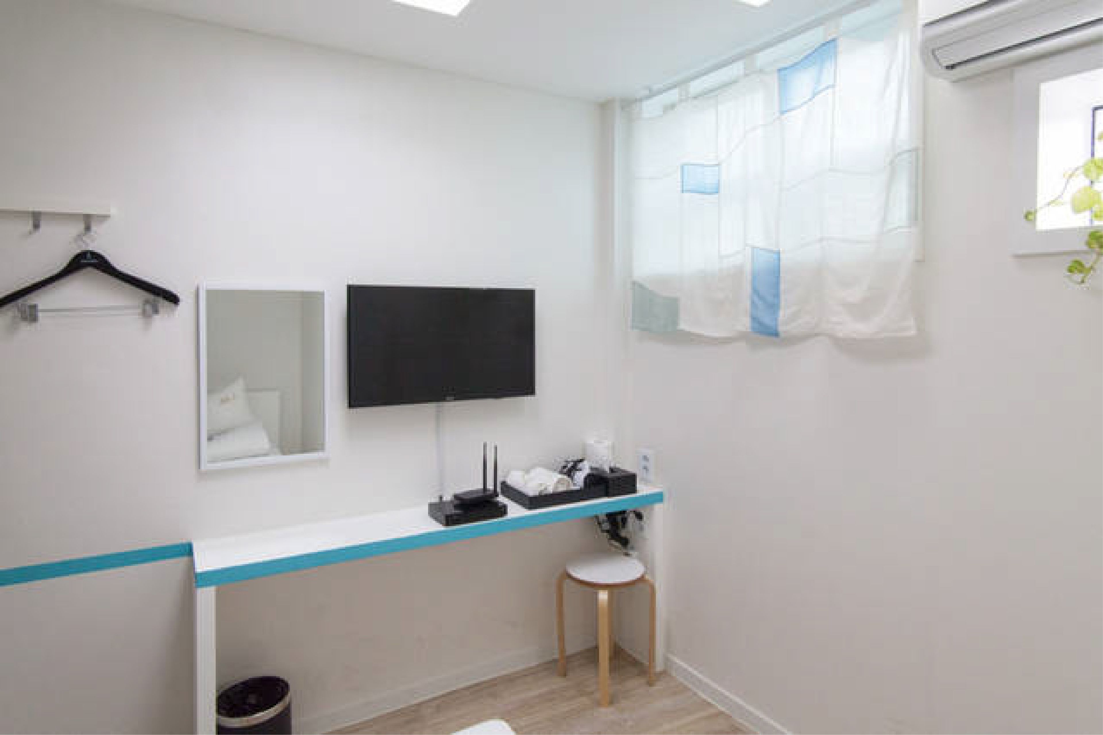 A small bathroom with a white sink, a mirror, a black television, and a window with a sheer curtain.