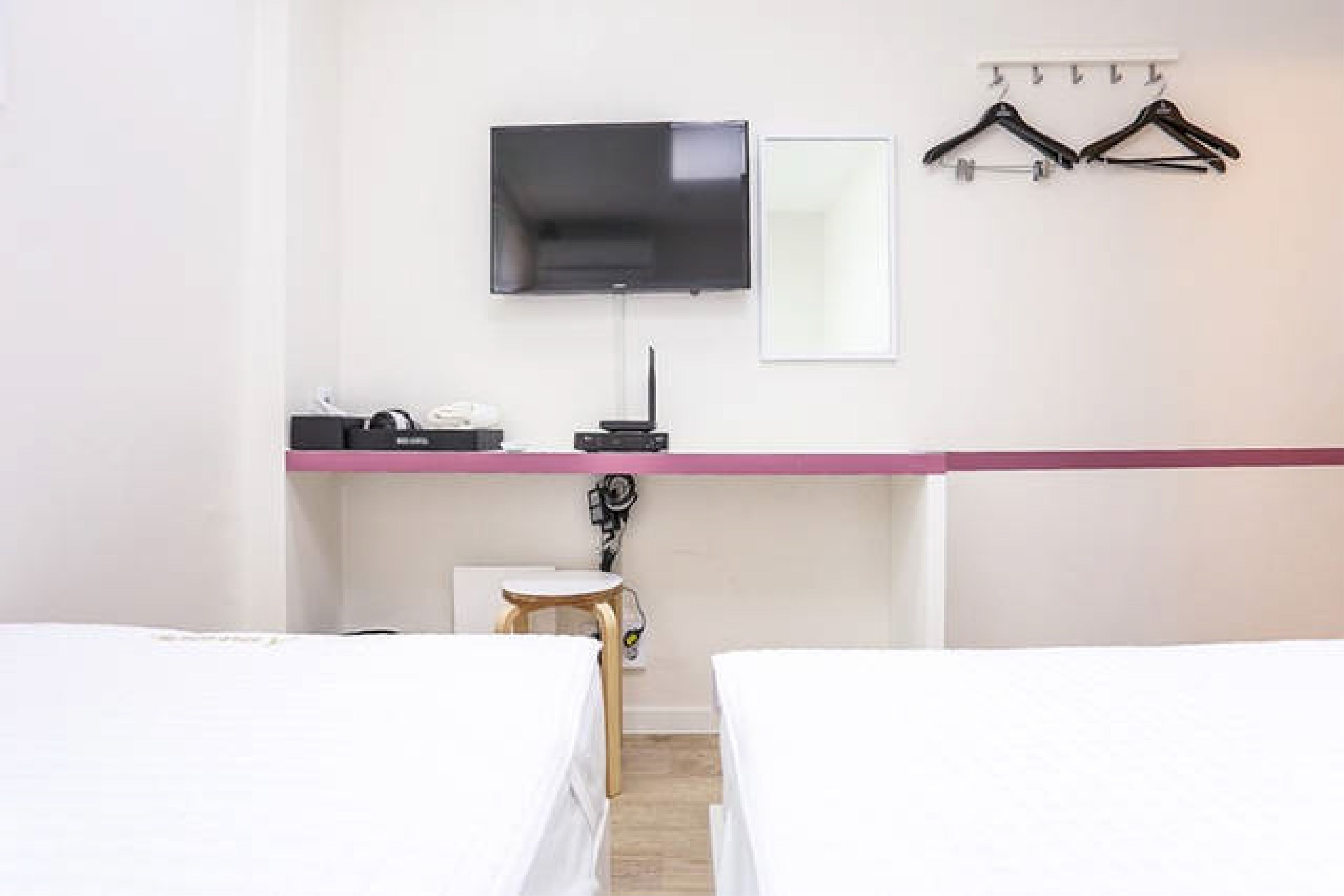 A hotel room with two beds, a flat-screen TV, a mirror, a desk with a computer, and a coat rack.