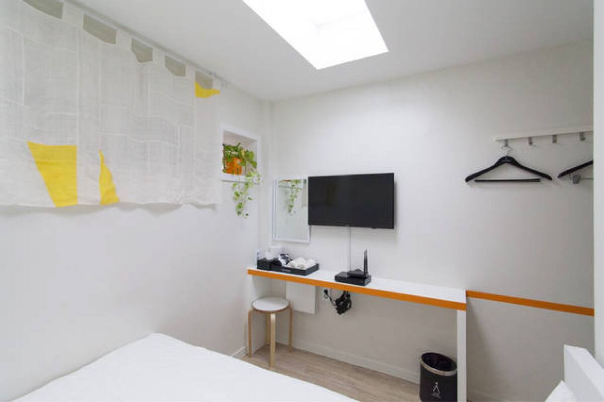 A bedroom with a bed, a desk with a chair, a TV, and a hanging clothes rack.