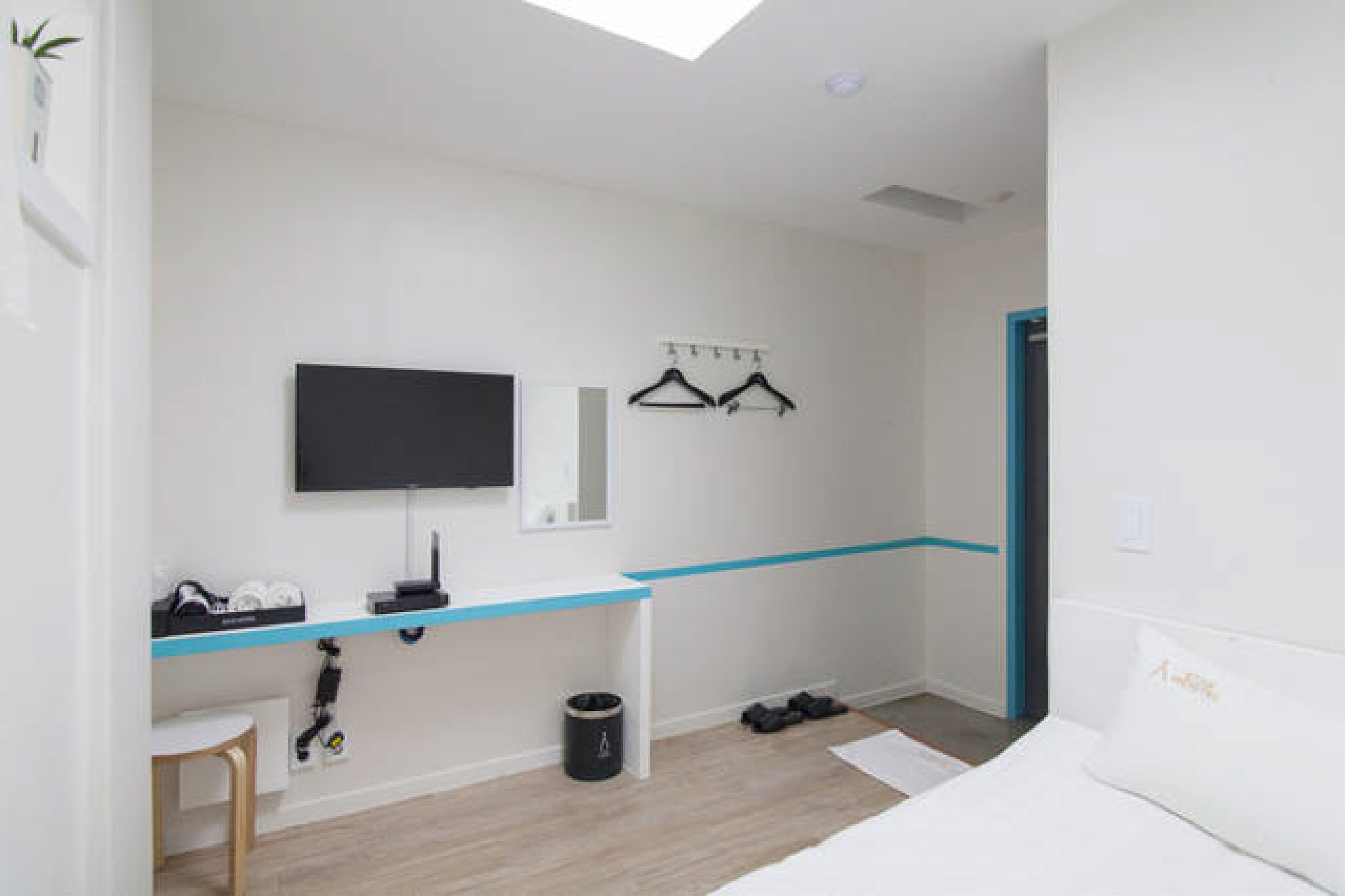 Ein modernes Schlafzimmer mit Oberlicht, einem an der Wand montierten Fernseher, einem Schreibtisch mit Stuhl und einem Bett mit Kissen.