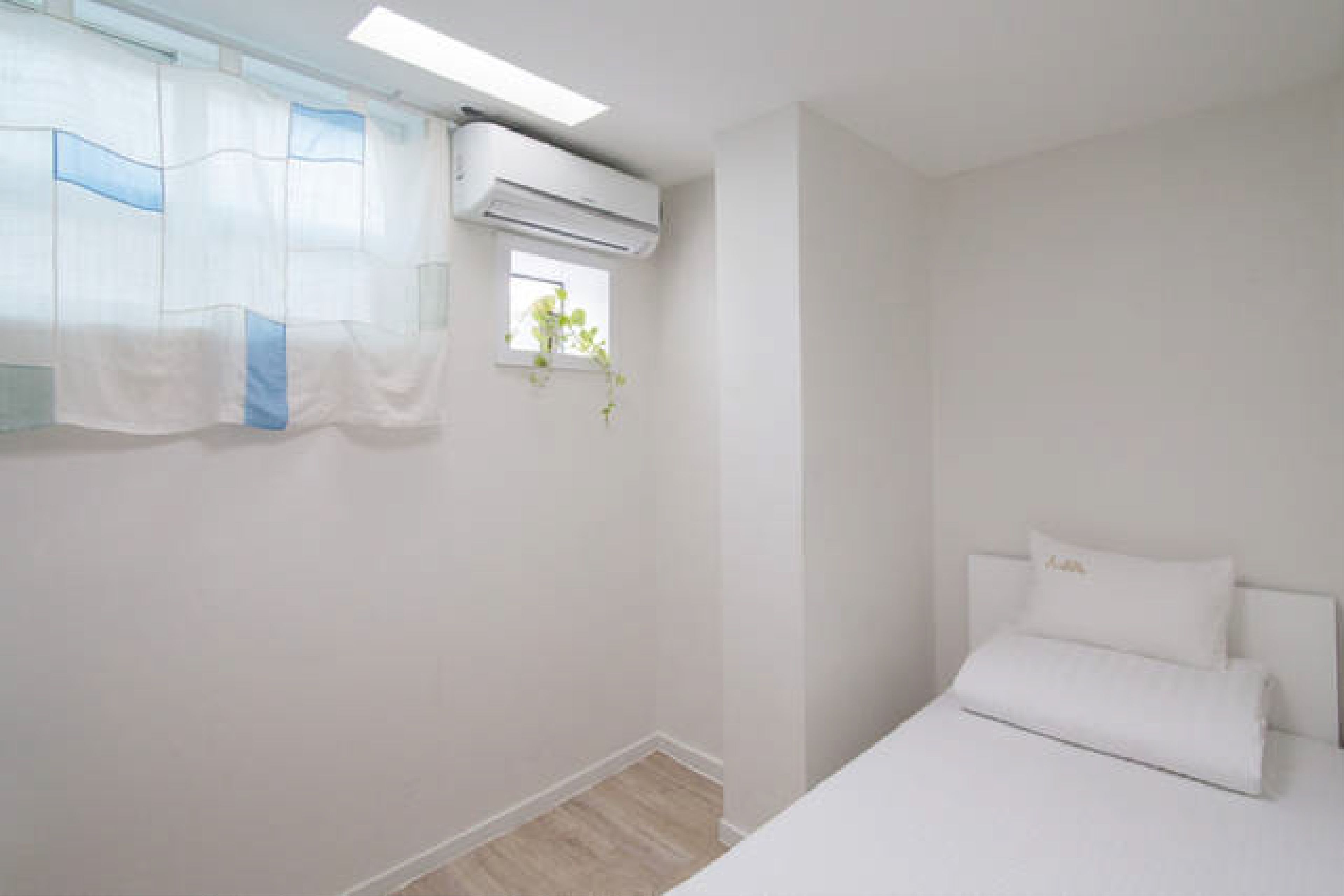 Quarto minimalista com cama, paredes brancas e aparelho de ar condicionado.