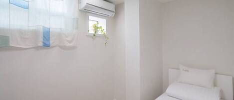 Quarto minimalista com cama, paredes brancas e aparelho de ar condicionado.