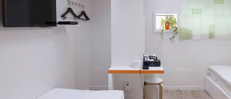 A small, clean room with a bed, a desk, a chair, a TV, and a window with a plant.