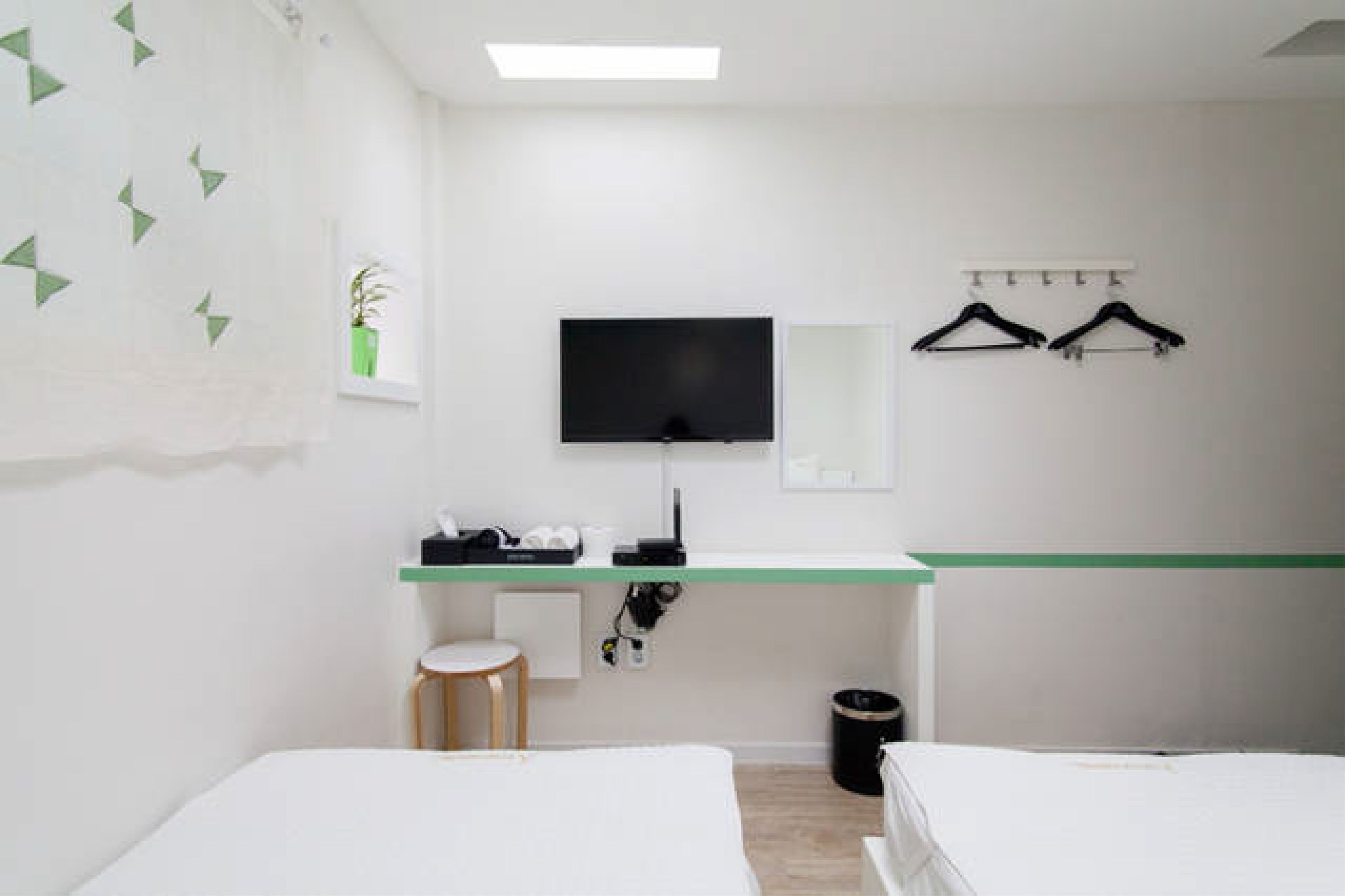 A hotel room with a bed, a desk with a flat-screen TV, a mirror, and a coat rack.