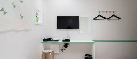 A hotel room with a bed, a desk with a flat-screen TV, a mirror, and a coat rack.