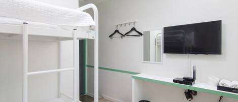 A bunk bed, a TV, a mirror, and a small desk with a trash can in a hotel room.