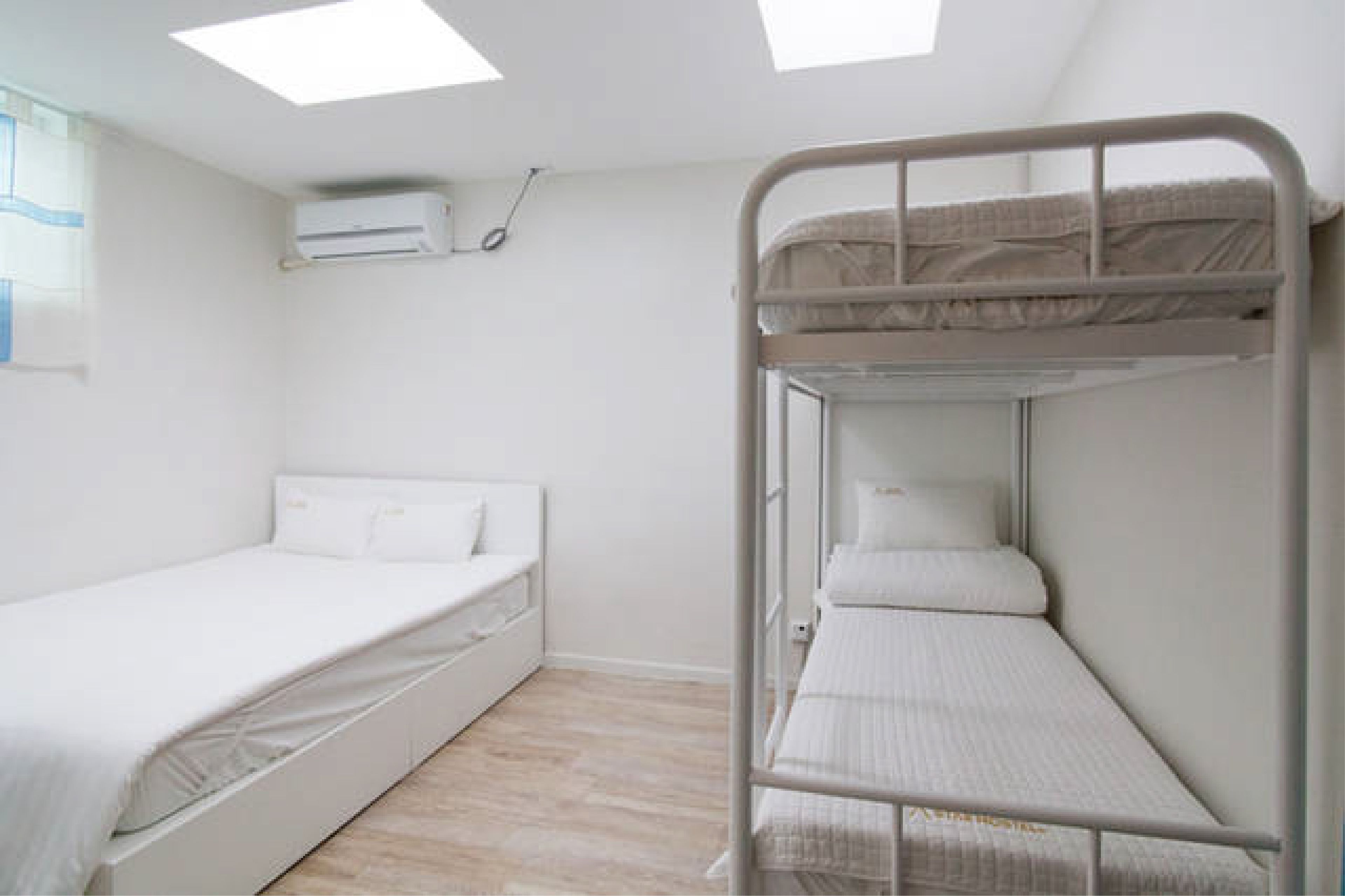 A room with a bunk bed, a single bed, and an air conditioning unit on the wall.