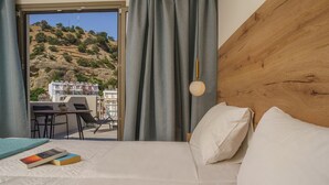 A hotel room with a bed, a desk, and a view of a hillside. - Sunlight Hotel (Agios Vasileios)