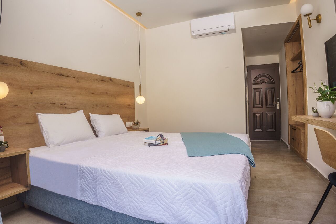 Een slaapkamer met een houten hoofdbord, een bed met wit beddengoed, een nachtkastje met een lamp en een kleine kamerplant.