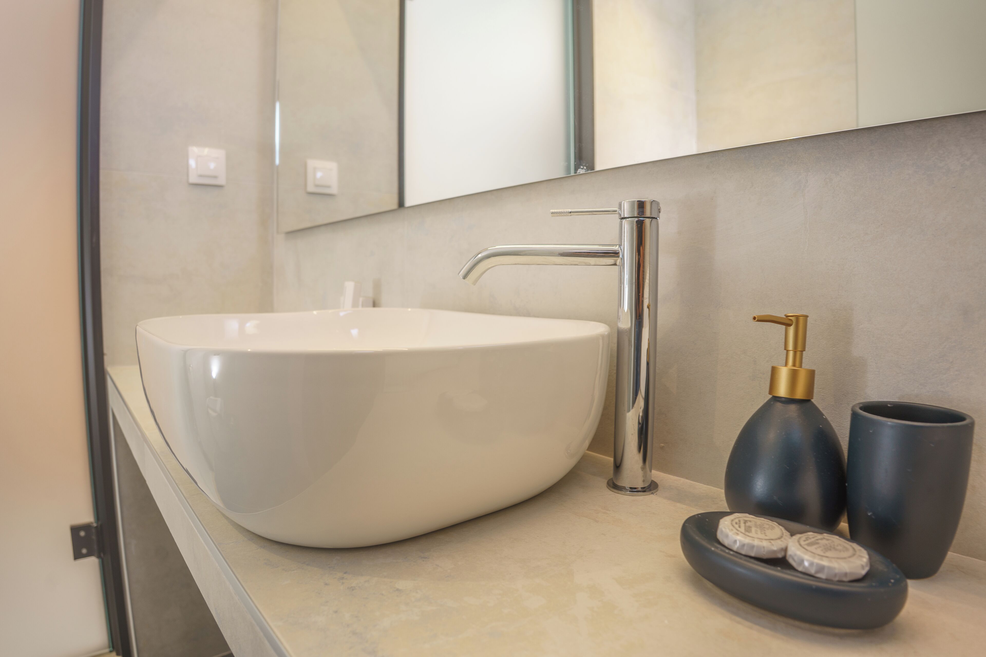 Ein modernes Badezimmer mit einem großen weißen Waschbecken, einem Chromarmaturen-Set und einem Seifenspender in dunkler Farbe.