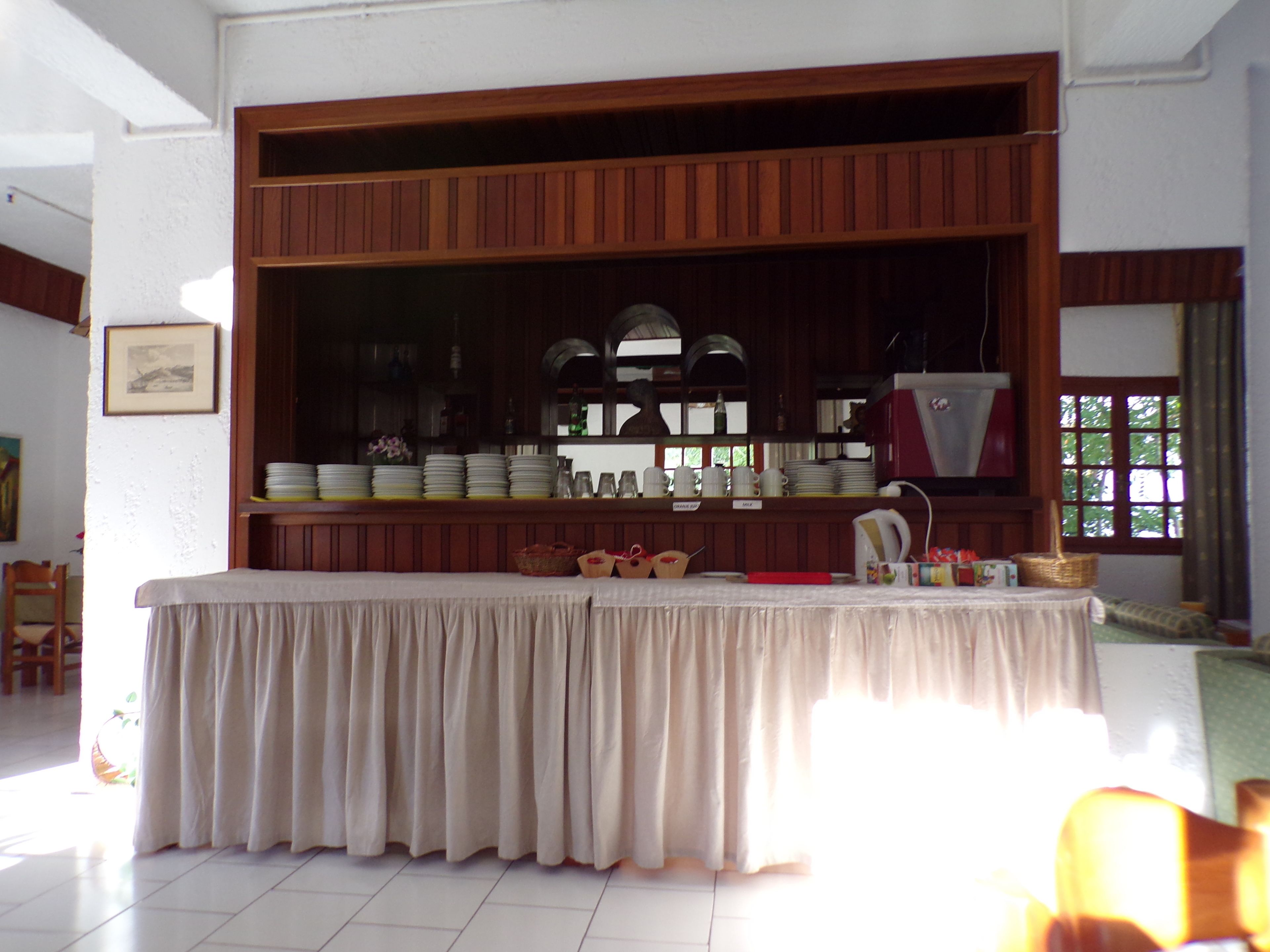A buffet setup with a table covered in a white cloth, surrounded by wooden cabinets with glass doors displaying plates, cups, and other dishes.