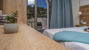 A bedroom with a bed, a wooden table, a potted plant, a nightstand, and a view of the outdoors. - Sunlight Hotel (Agios Vasileios)