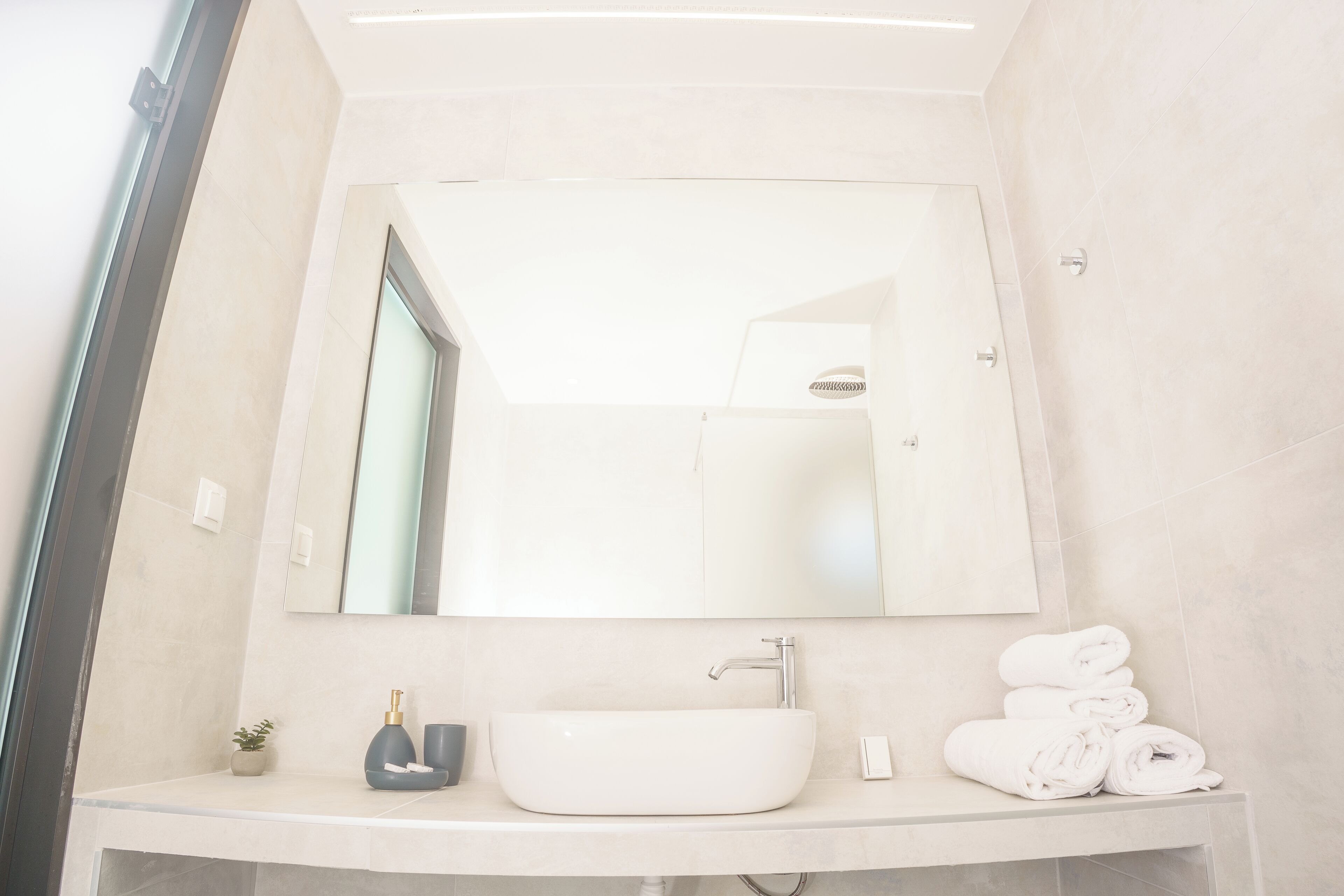 A modern bathroom with a large mirror, a white sink, and a towel stack.
