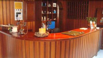Un mostrador de recepción con detalles de madera, una pizarra con anuncios y un estante con diversos objetos.