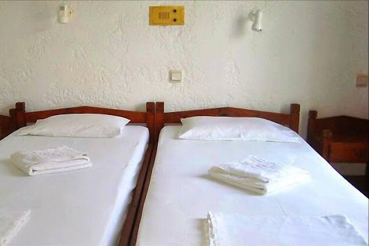 Habitación doble con dos camas, cada una con colchón y almohadas blancos, cabeceros de madera y mesitas de noche.