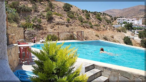 A swimming pool with a stone wall and a view of a hillside with buildings. - Sunlight Hotel (Agios Vasileios)