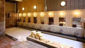 A public sauna with multiple wooden benches and individual shower stalls, each with a mirror and overhead lighting. - Hotel Yudanaka (Yamanouchi)