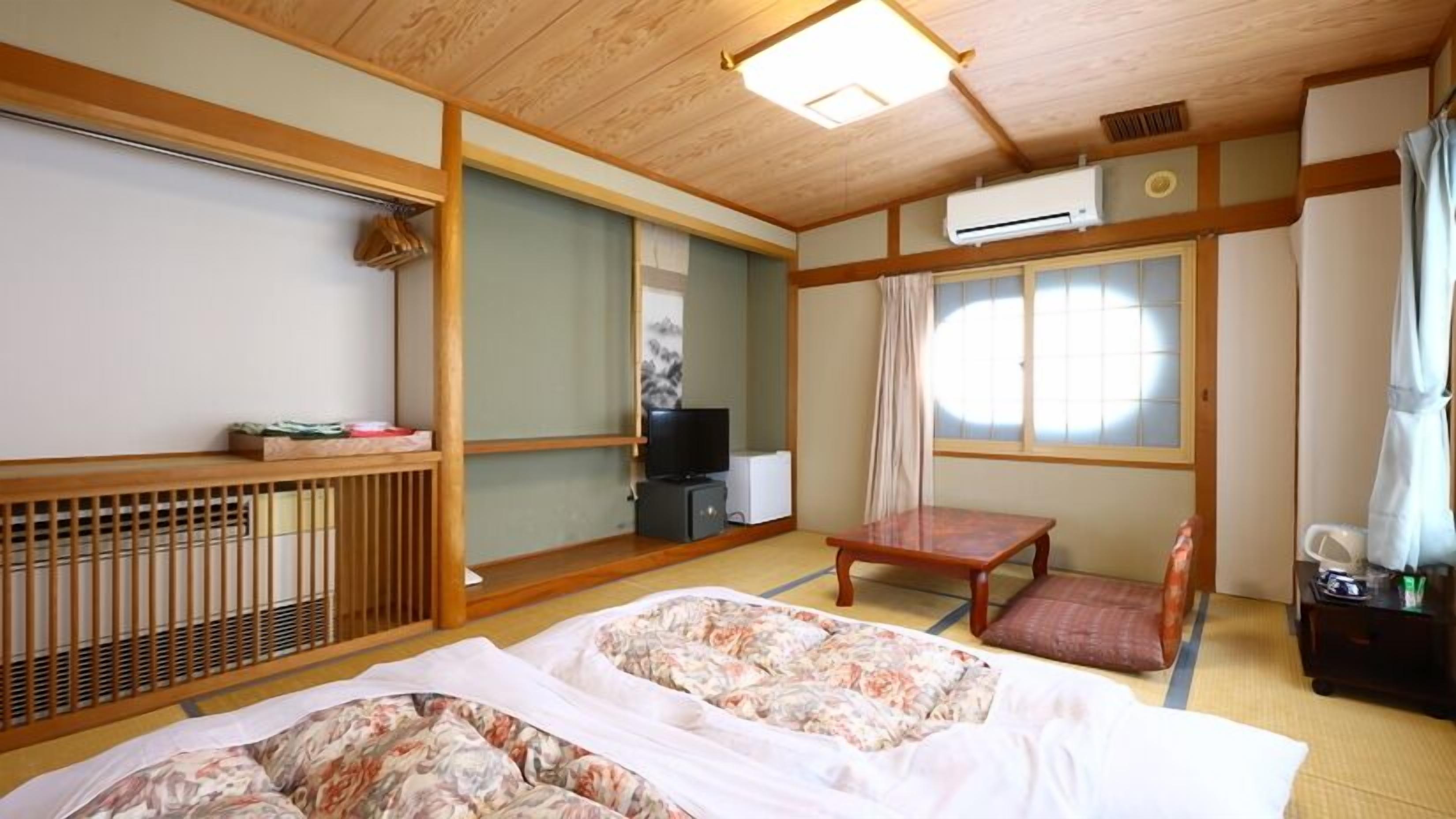 A traditional Japanese-style room with tatami flooring, a futon bed, a television, a small table, and a sliding door.