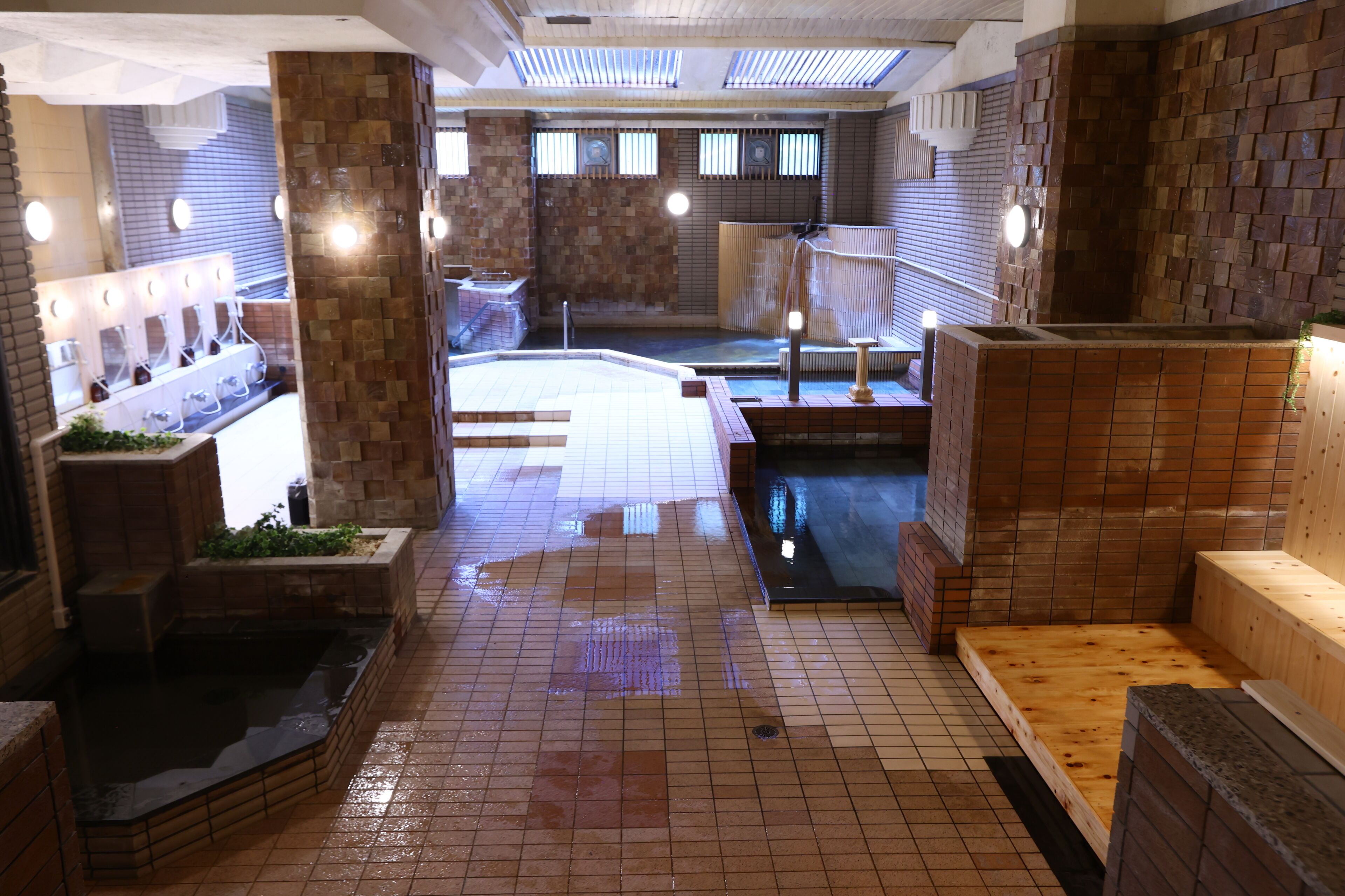 A traditional Japanese onsen with multiple hot spring baths, wooden benches, and tiled flooring.