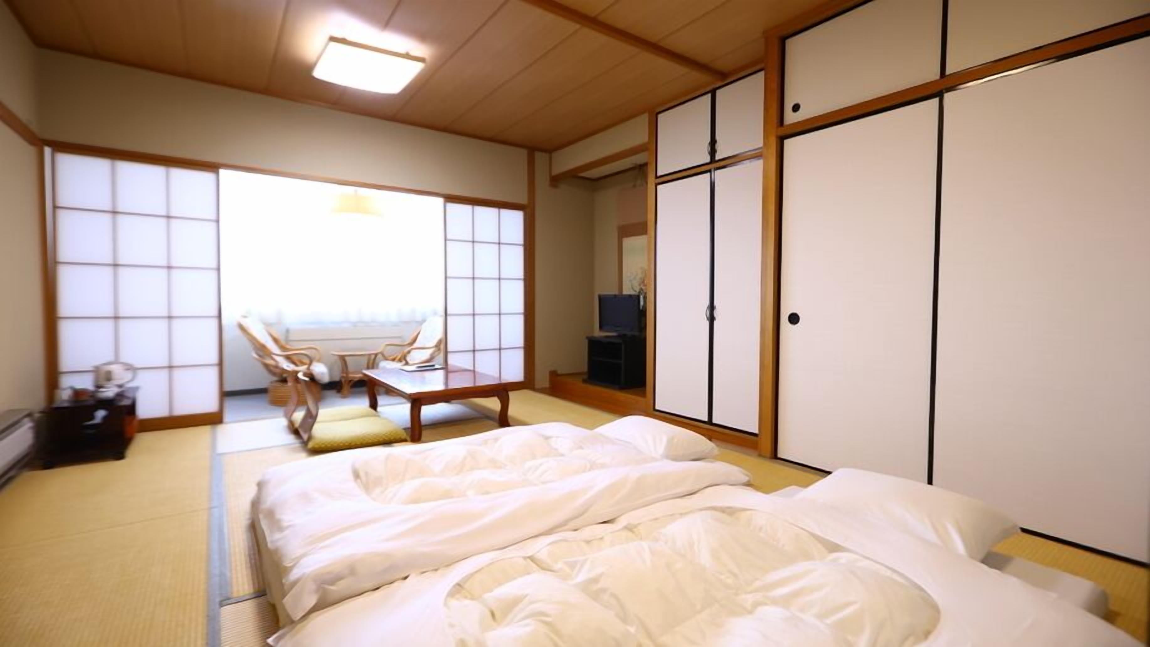 A traditional Japanese room with tatami flooring, a futon bed, a low table with chairs, and sliding doors.