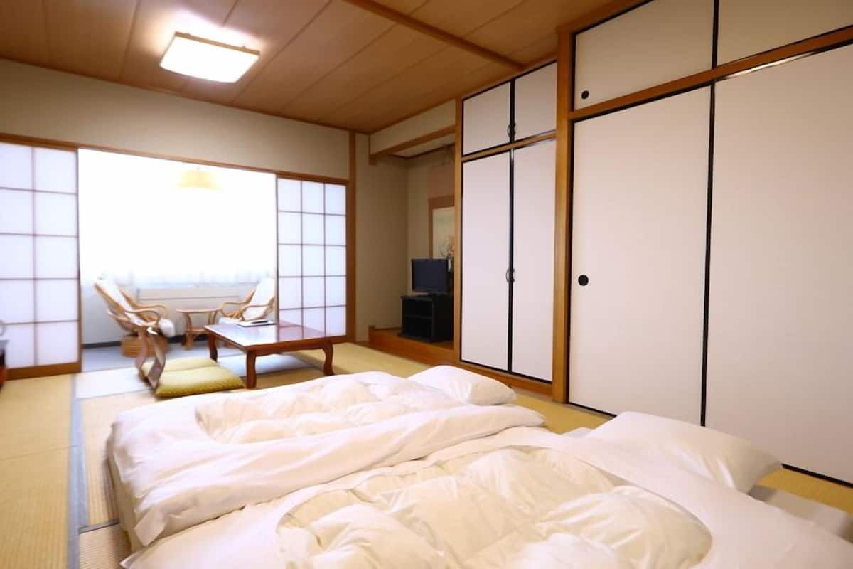 A traditional Japanese room with tatami flooring, a futon bed, a low table with chairs, and sliding doors.