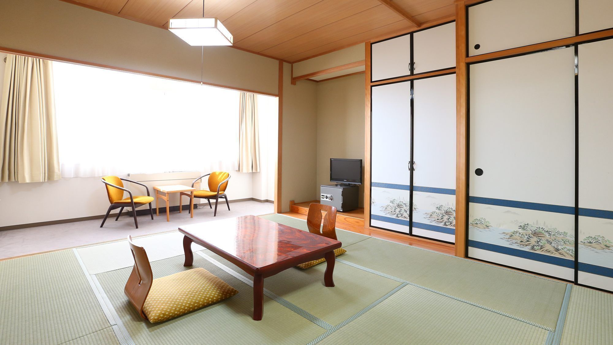 A traditional Japanese room with tatami flooring, a low table, chairs, a television, and sliding doors with decorative patterns.