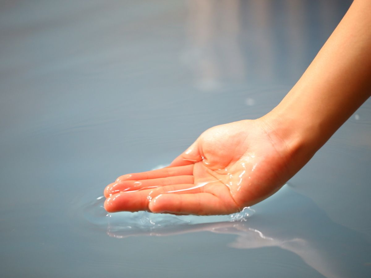 A hand with water droplets on a smooth surface.