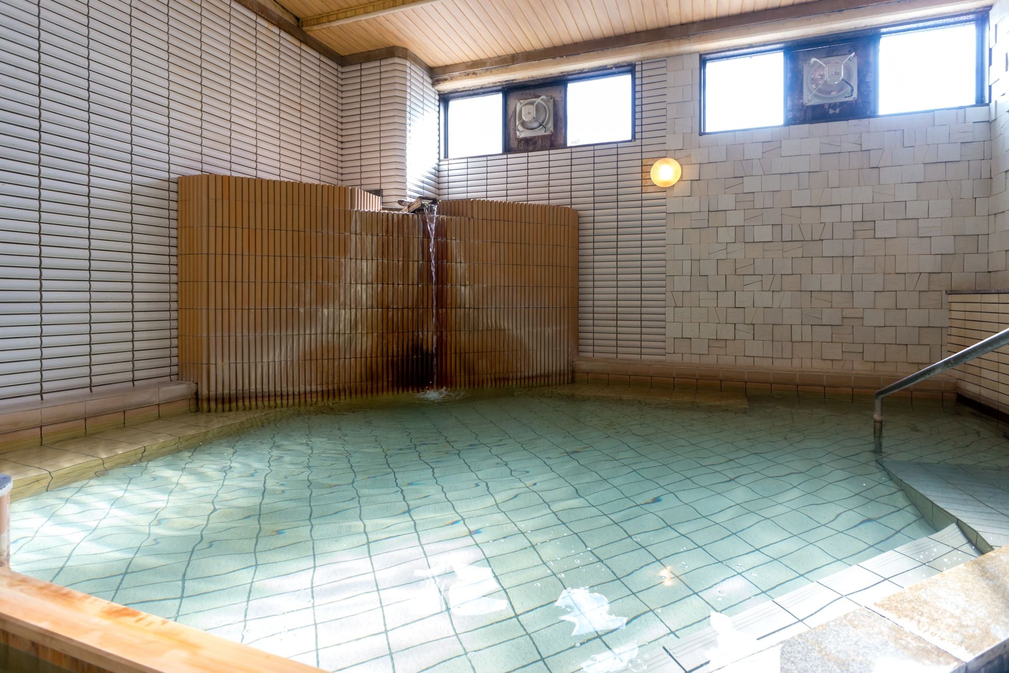 A traditional Japanese onsen with a tiled floor, wooden benches, and a wooden sliding door.