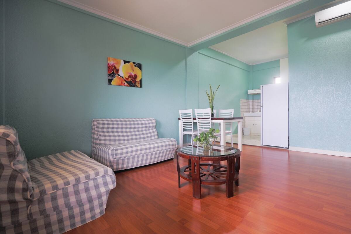 A living room with a checkered sofa, a round wooden table with chairs, and a painting on the wall.