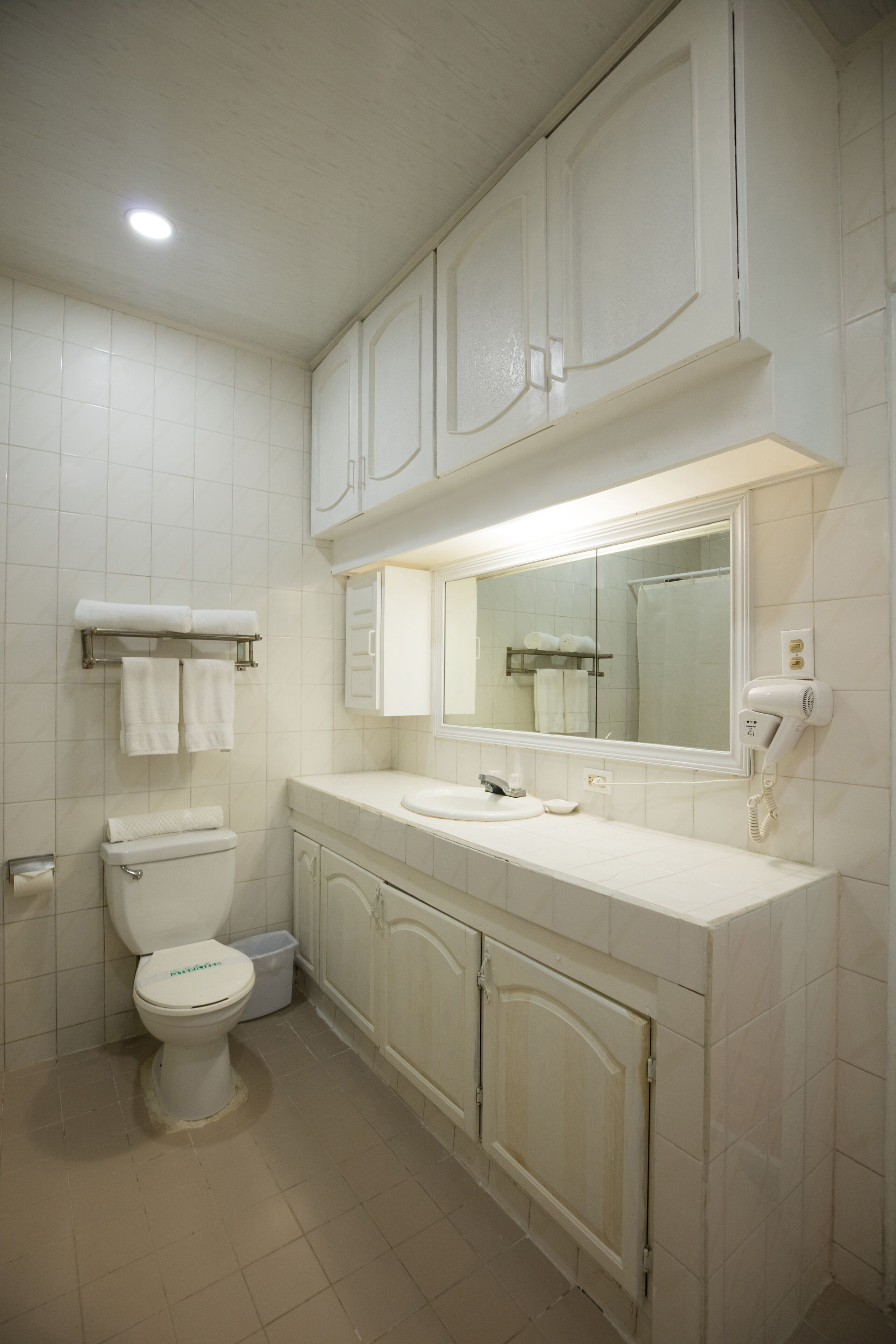 A bathroom with a toilet, sink, mirror, and cabinets.