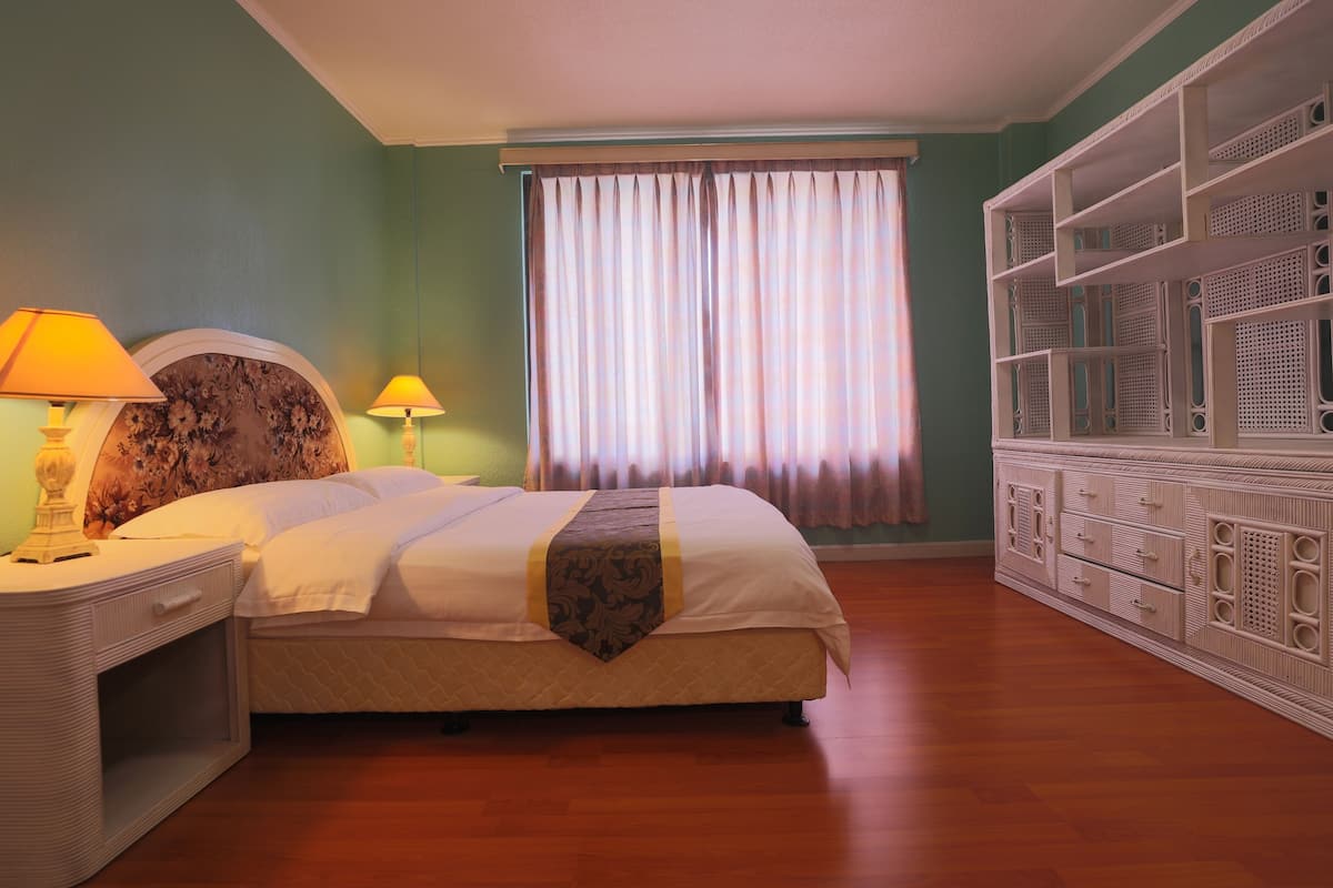 A bedroom with a bed, nightstands, a dresser, and a window with curtains.