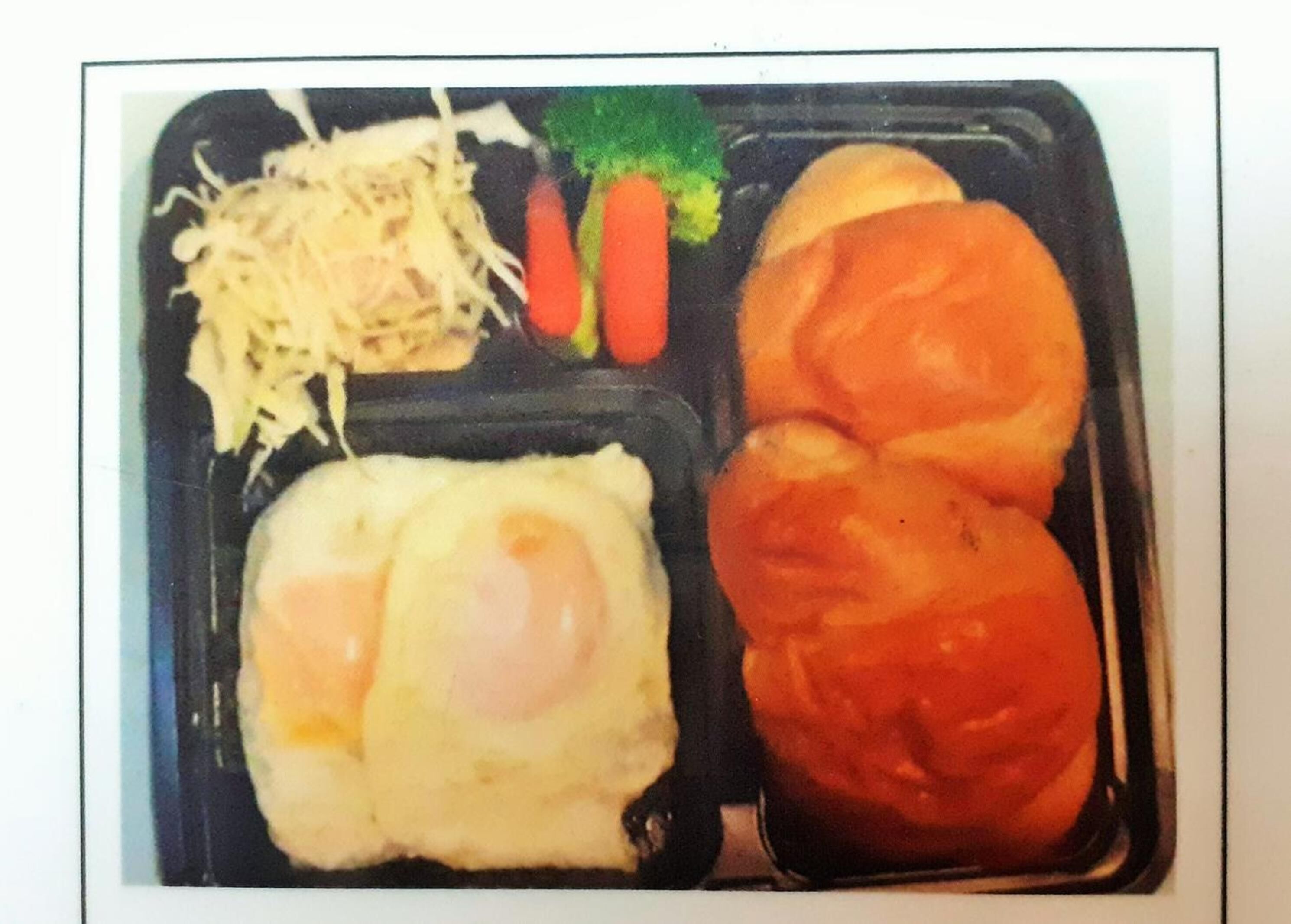 A meal with a fried egg, sausage, cheese, carrots, and broccoli in a black tray.