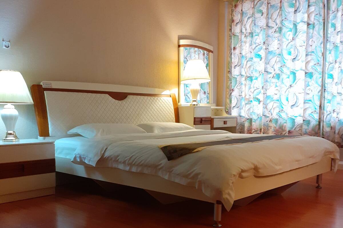 A hotel room with a bed, nightstands, a lamp, and a window with curtains.