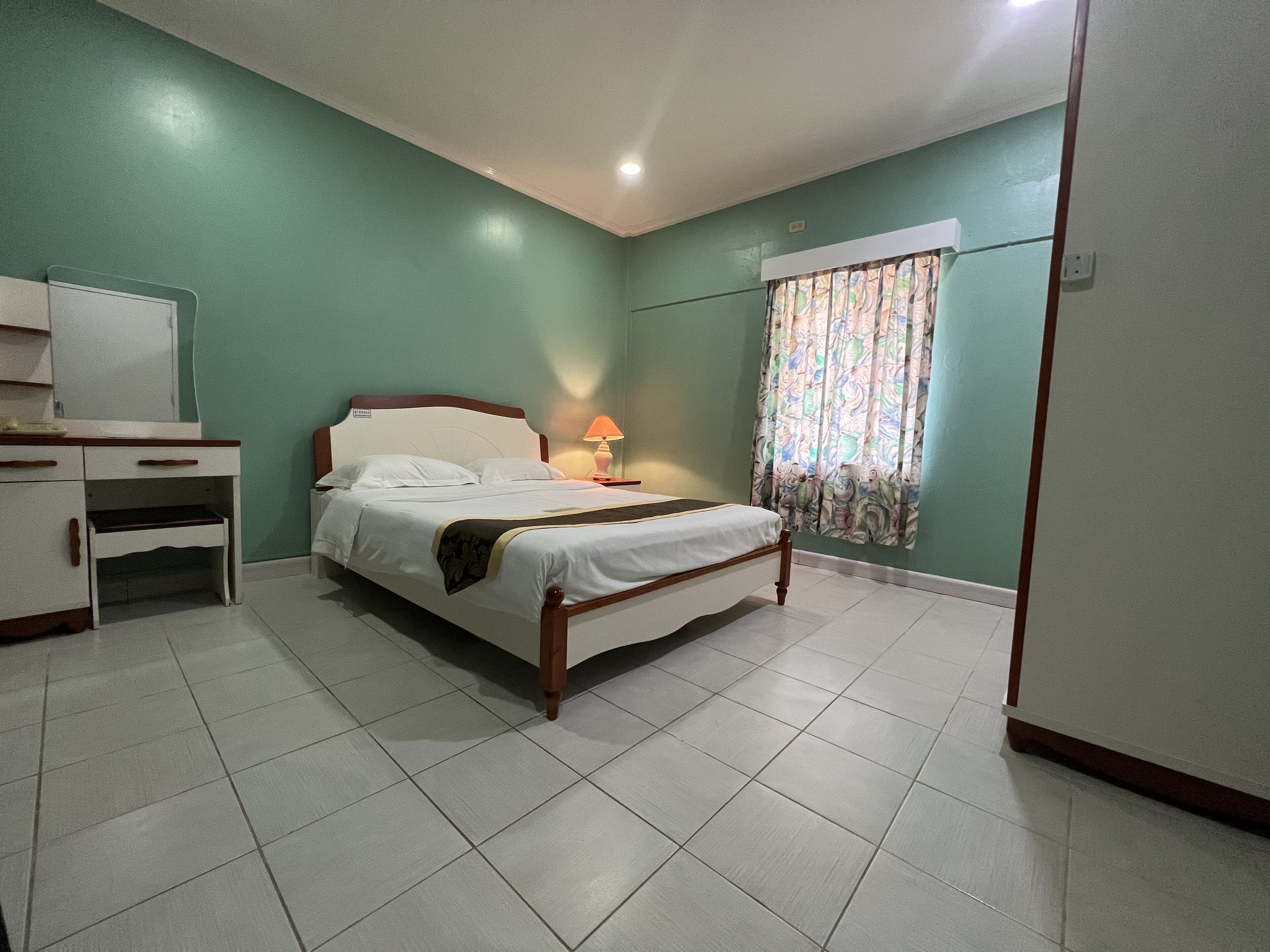Un dormitorio ordenado con cama, mesita de noche, lámpara y escritorio con cajones.