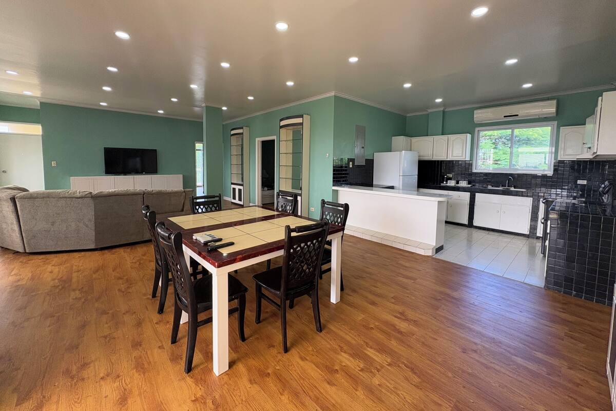 A spacious living area with a dining table, sofa, and kitchen with white cabinets and a black countertop.