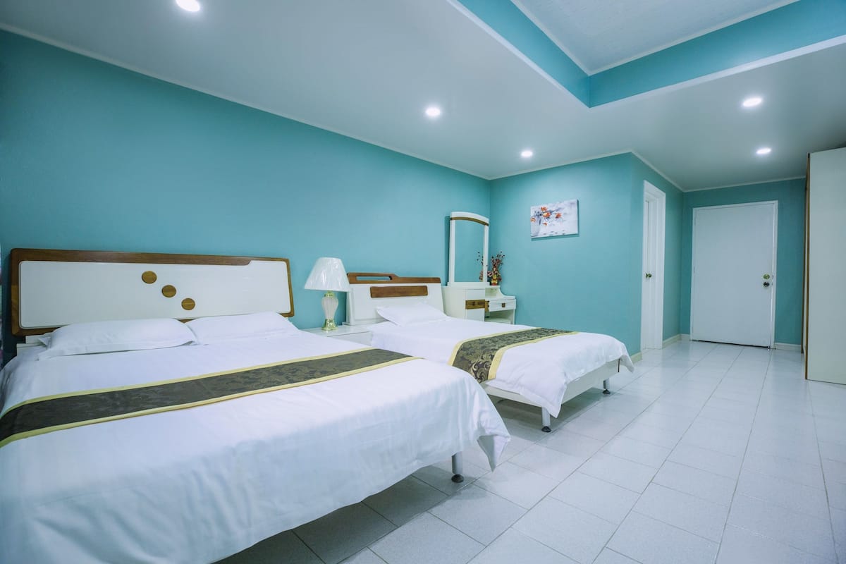 A hotel room with two beds, a nightstand, a lamp, a mirror, and a door.