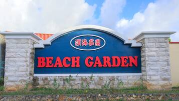A sign for a beach garden with a stone wall and a clear blue sky in the background.